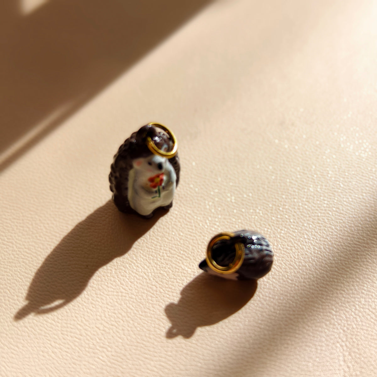 Actual Flower Keeper and Sleepy Bramble hedgehog charms together, showing the taller flower-holding charm and smaller curled companion