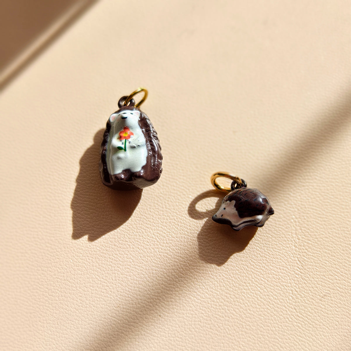 Actual mother-and-child inspired hedgehog charm pair in natural sunlight, with gold-tone attachment rings