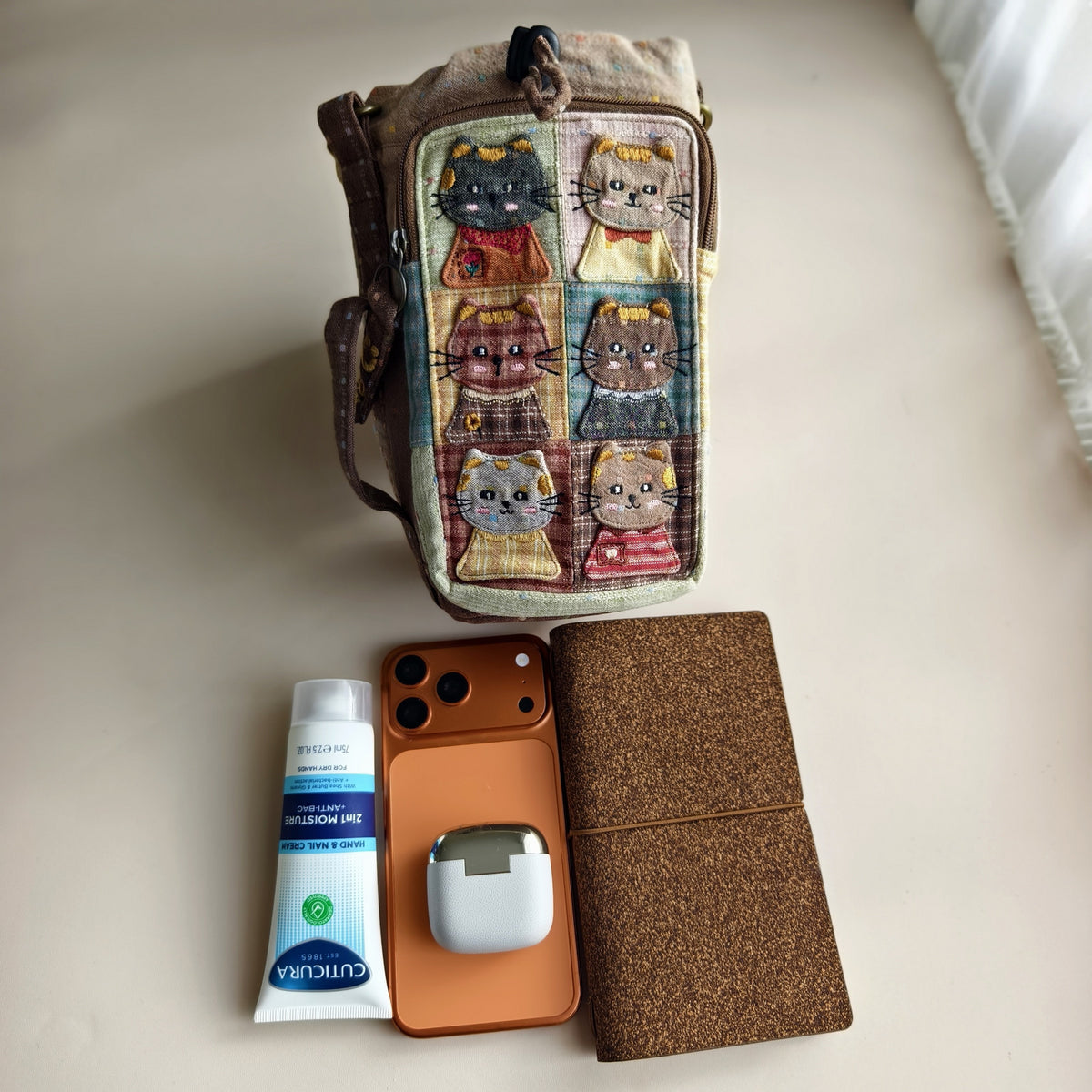 Actual bag beside a phone, notebook, earbuds and hand cream for size context; props not included