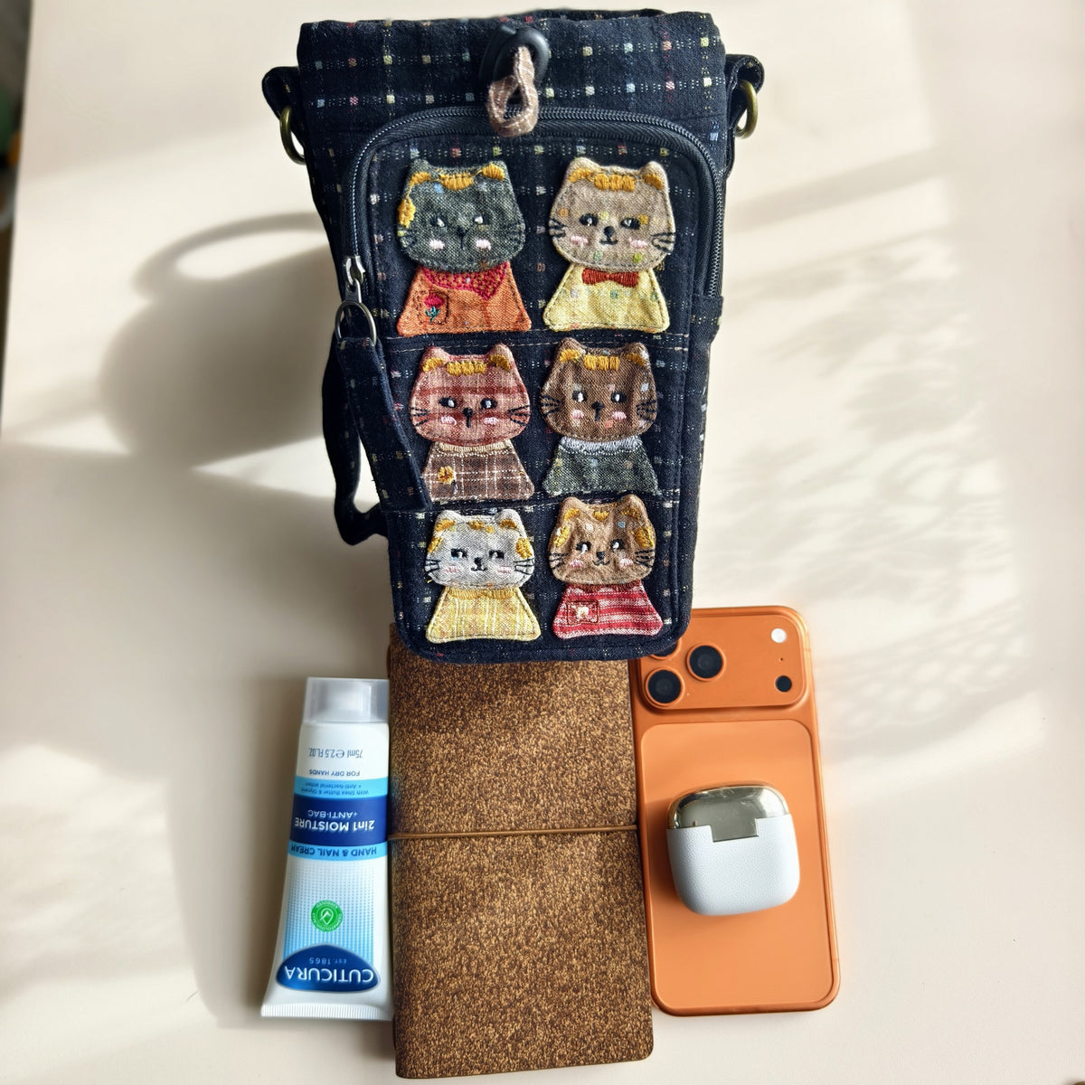 Actual navy bag beside a phone, notebook, earbuds and hand cream; props not included