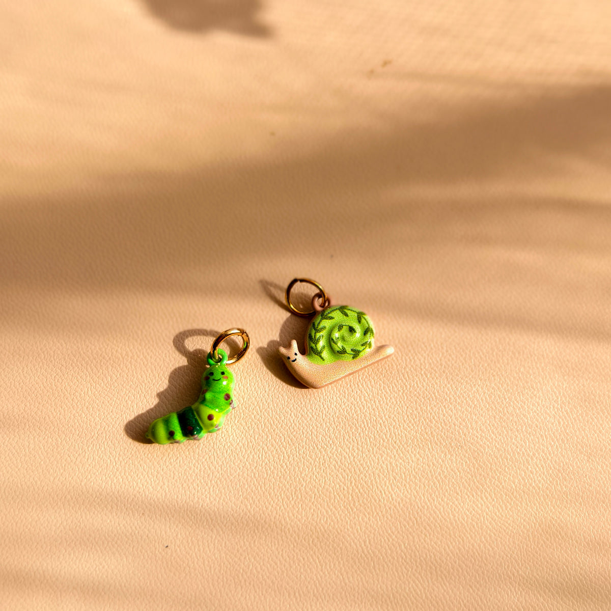 Actual Clover Caterpillar and Ivy Trail Snail charms together on a cream surface